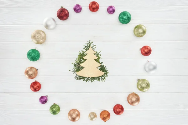 Vue de dessus des brindilles de conifères, symbole d'arbre de Noël et boules brillantes colorées sur la surface en bois — Photo de stock