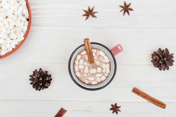 Vista superior do copo com chocolate quente e marshmallows, paus de canela, anis estrelado e cones de pinho na mesa de madeira — Fotografia de Stock