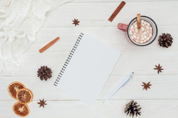 Plat posé avec bloc-notes vierge et tasse de chocolat chaud, guimauves et bâtonnets de cannelle sur table en bois — Photo de stock