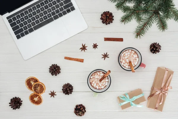 Flache Liege mit Laptop, Tassen mit heißer Schokolade und Weihnachtsgeschenken auf Holztisch — Stockfoto