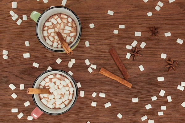 Draufsicht auf Tassen mit heißer Schokolade, Marshmallows und Zimtstangen auf Holztisch — Stockfoto