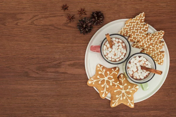 Tassen mit heißer Schokolade und Marshmallows, Zimtstangen und Lebkuchen auf Holztisch — Stockfoto