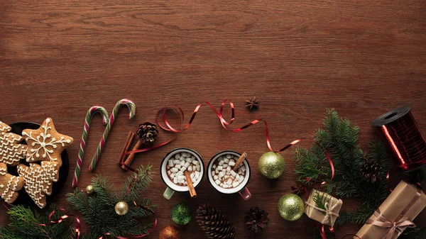 Vista superior de tazas con chocolate caliente, malvaviscos y palitos de canela y decoraciones de Navidad sobre fondo de madera — Stock Photo