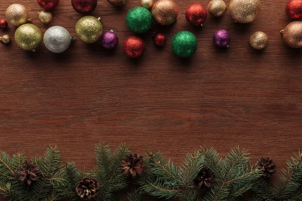 Vue de dessus des boules colorées brillantes et des brindilles de conifères avec des cônes de pin sur fond en bois — Photo de stock