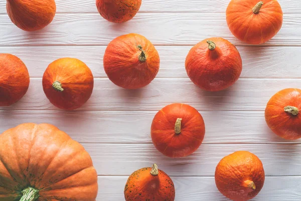 Blick von oben auf verstreute herbstliche orangefarbene Kürbisse auf hölzerner Tischplatte — Stockfoto