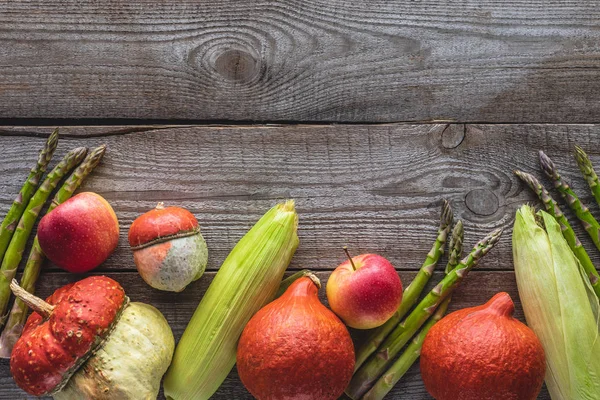 Vista superior de mazorcas de maíz, espárragos verdes, calabazas y manzanas sobre una mesa de madera gris - foto de stock