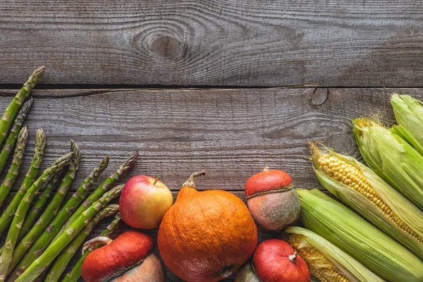 Elevated view of corn cobs, green asparagus, pumpkins and apple on grey wooden tabletop — Stock Photo