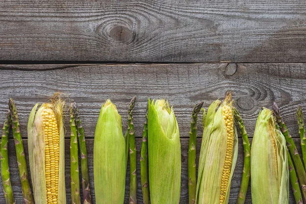 Vista dall'alto di pannocchie di mais mature e asparagi verdi su un tavolo di legno grigio — Foto stock