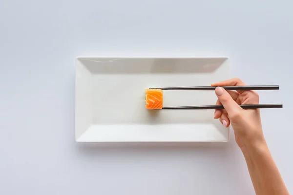 Tiro cortado de pessoa com pauzinhos segurando delicioso sushi na placa branca isolada no branco — Fotografia de Stock