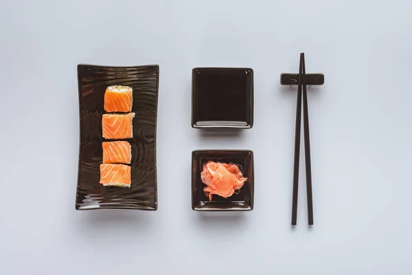 Blick von oben auf köstliches Sushi mit Lachs, Ingwer, Sojasauce und Essstäbchen isoliert auf weiß — Stockfoto