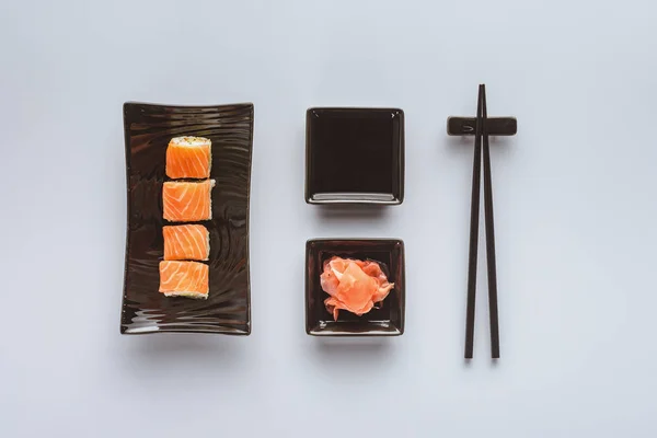 Top view of delicious sushi with salmon, ginger, soy sauce and chopsticks isolated on white — Stock Photo