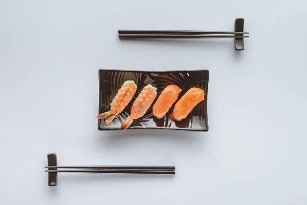 Vista superior de sushi sabroso con salmón y camarones en el plato y palillos aislados en blanco - foto de stock