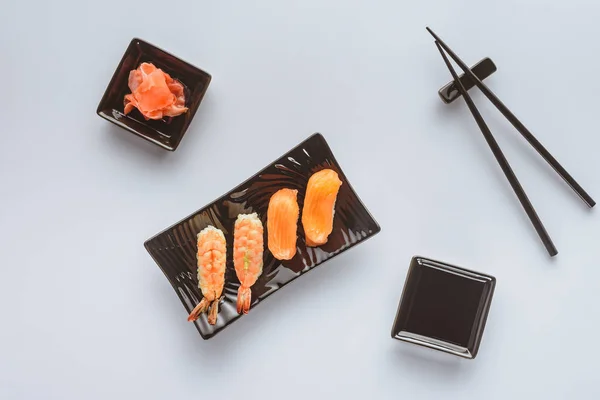 Draufsicht auf schmackhaftes Sushi mit Lachs und Garnelen, Ingwer und Essstäbchen isoliert auf weiß — Stockfoto