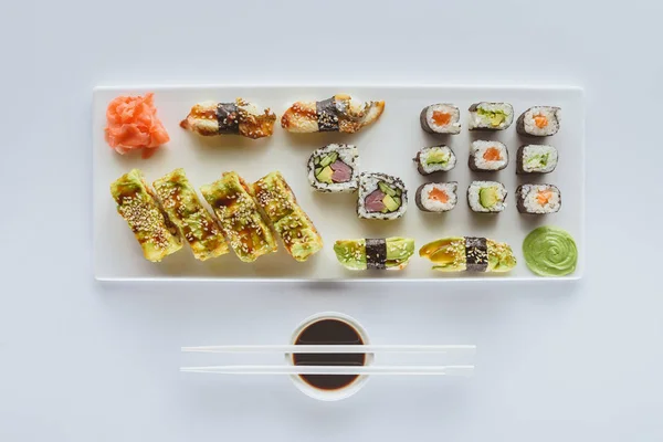 Top view of gourmet sushi set with ginger, wasabi, soy sauce and chopsticks isolated on white — Stock Photo