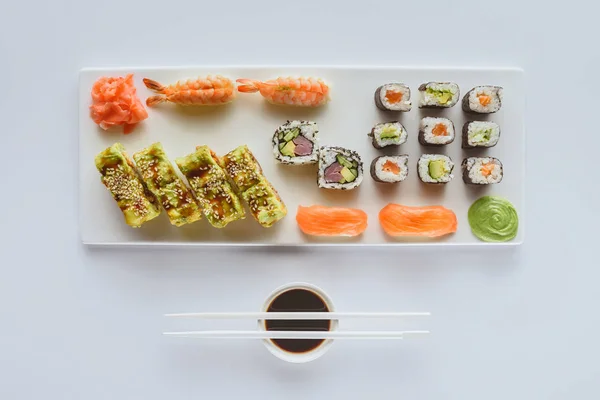 Vista superior de sushi delicioso conjunto con jengibre, wasabi, salsa de soja y palillos aislados en blanco - foto de stock