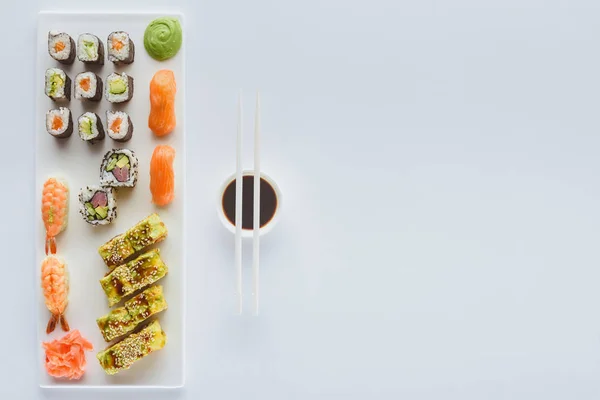 Top view of delicious sushi set and soy sauce in bowl with chopsticks isolated on white background — Stock Photo