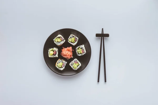 Top view of delicious sushi with ginger on round plate and chopsticks isolated on white — Stock Photo