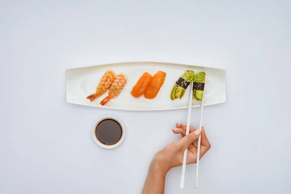 Vista superior parcial de la persona sosteniendo palillos y comiendo sushi delicioso aislado en blanco - foto de stock