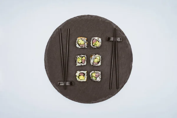 Вид сверху на вкусные суши и палочки для еды на круглой доске, изолированной на белом — стоковое фото