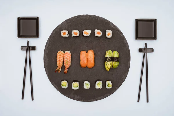 Vista superior de vários deliciosos sushi em tábua de ardósia e pauzinhos isolados em branco — Fotografia de Stock