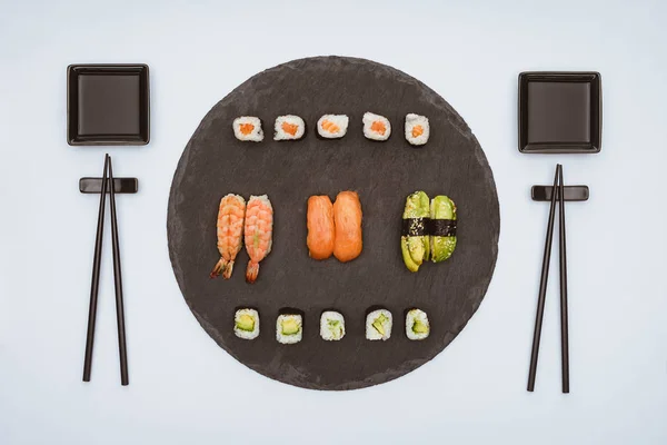 Вид сверху на различные вкусные суши на доске и палочки для еды, изолированные на белом — стоковое фото