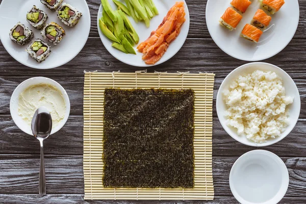 Vista dall'alto di nori e deliziosi ingredienti per cucinare sushi sul tavolo di legno — Foto stock