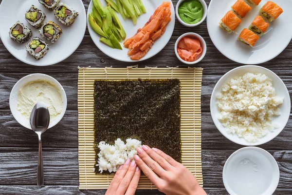 Partial top view of person preparing sushi with rice, nori and ingredients — Stock Photo