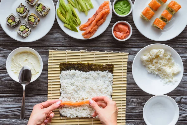 Cropped shot of person cooking delicious sushi roll with salmon, rice and nori — Stock Photo