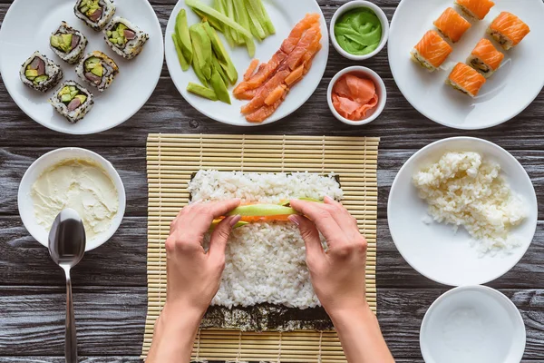 Tiro cortado de pessoa cozinhar delicioso rolo de sushi com salmão, abacate e pepino — Fotografia de Stock