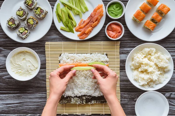 Cropped shot of person preparing sushi with salmon and avocado — Stock Photo