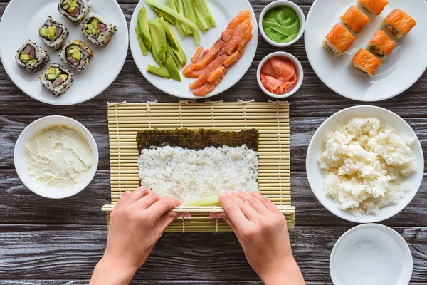 Tiro recortado de la persona preparando sushi con arroz y nori - foto de stock