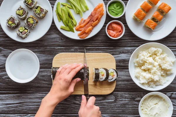 Частичный вид сверху на человека, резающего вкусный суши-ролл ножом — стоковое фото