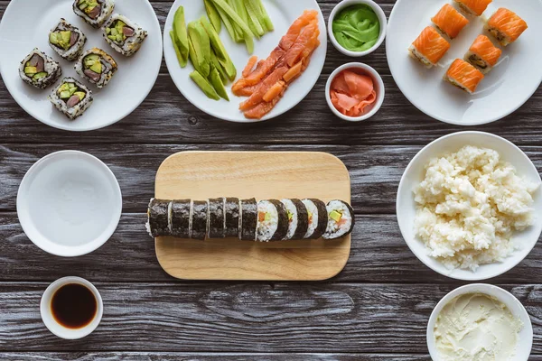 Top view of delicious sliced sushi roll and ingredients on wooden table — Stock Photo