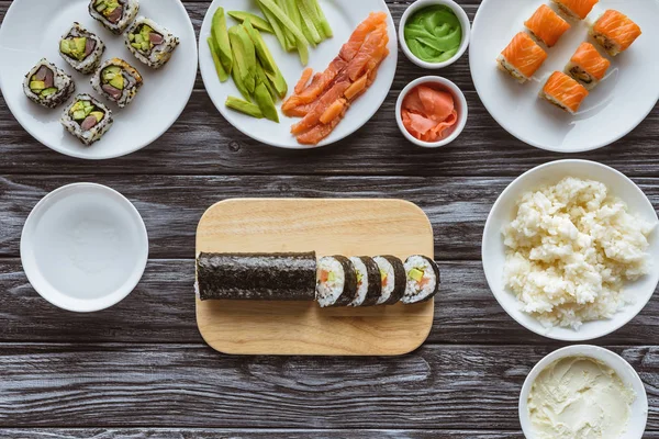 Top view of delicious sushi rolls and ingredients on wooden table — Stock Photo