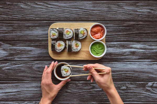 Vista dall'alto parziale di persona che tiene le bacchette e mangia delizioso rotolo di sushi — Foto stock