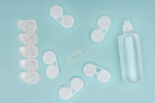 Deitado plano com líquido estéril em garrafa, pinças e recipientes para armazenamento de lentes de contato em mesa azul — Fotografia de Stock