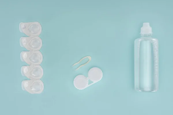 Плоский шар зі стерильною рідиною в пляшці, пінцетом і контейнерами для контактних лінз на синій стільниці — стокове фото