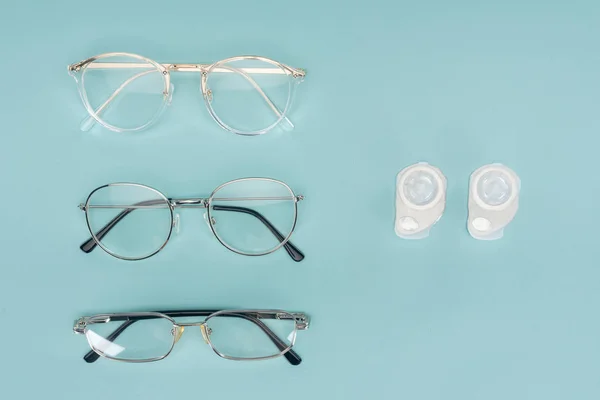 Top view of eyeglasses and contact lenses containers arranged on blue background — Stock Photo