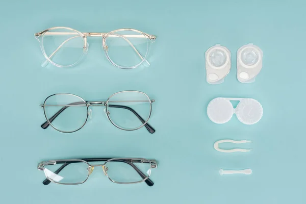 Vista superior de óculos, lentes de contato recipientes e pinças dispostas sobre fundo azul — Fotografia de Stock