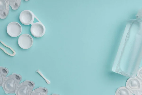 Flat lay with sterile liquid in bottle, tweezers and containers for contact lenses on blue tabletop — Stock Photo