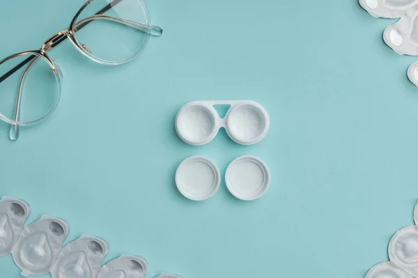 Top view of eyeglasses and arranged contact lenses containers on blue background — Stock Photo