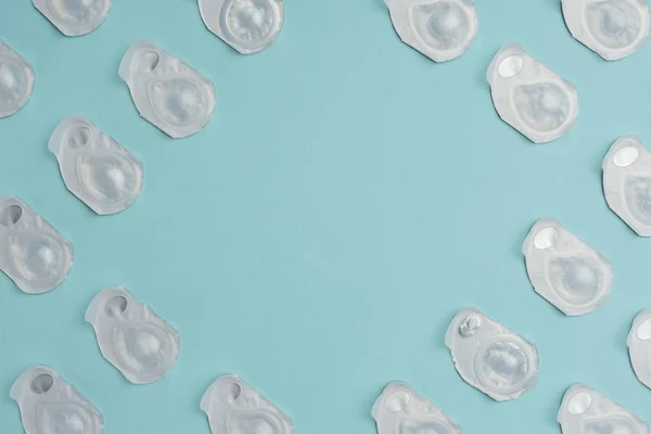 Flat lay com lentes de contato em recipientes dispostos em fundo azul com espaço em branco no meio — Fotografia de Stock