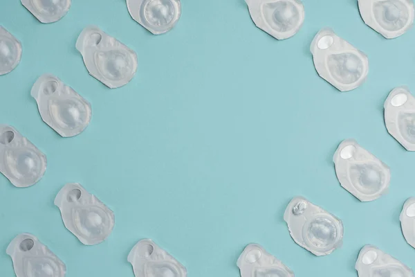 Flat lay with contact lenses in containers arranged on blue background with blank space in middle — Stock Photo