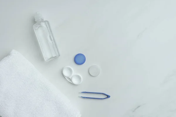 Flache Liege mit Handtuch, Kontaktlinsenaufbewahrungsgeräte auf weißer Tischplatte angeordnet — Stockfoto