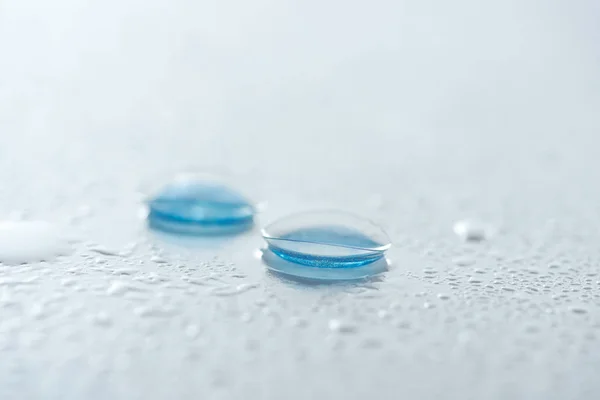 Vista de cerca de las lentes de contacto sobre fondo blanco con gotas de agua - foto de stock