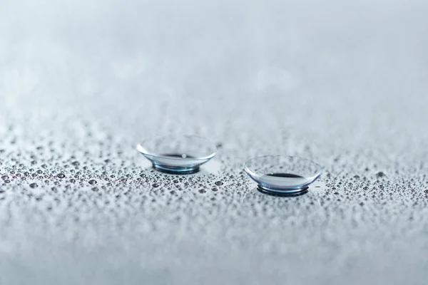 Vista de cerca de las lentes de contacto en el fondo con gotas de agua - foto de stock