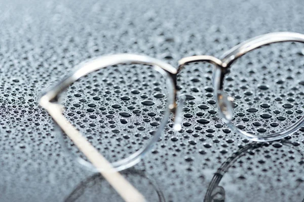 Vista de cerca de las gafas y gotas de agua sobre fondo gris - foto de stock