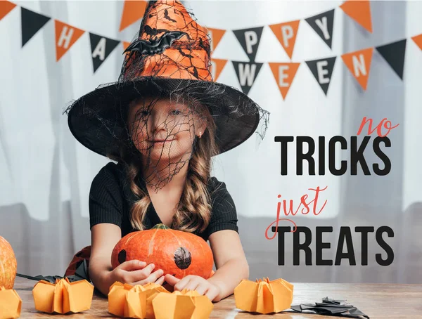 Retrato de criança adorável em trajes de bruxa halloween na mesa com abóboras em casa com letras 