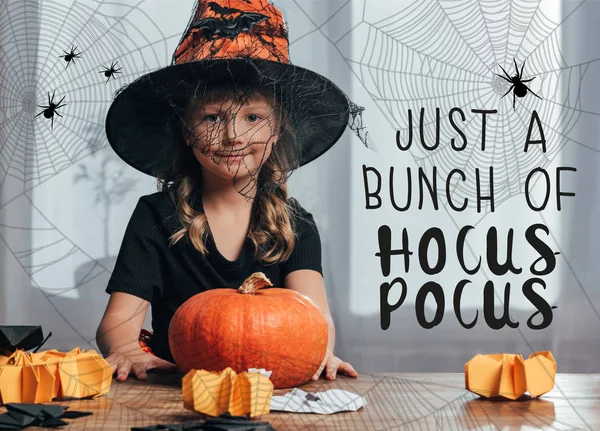 Retrato de niño adorable en disfraz de bruja Halloween sentado en la mesa con calabaza en casa con letras de 
