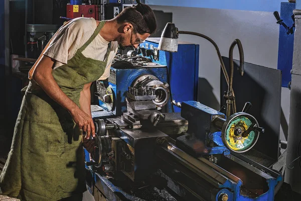 Visão lateral do trabalhador da fabricação masculina no avental protetor e nos óculos usando a máquina-ferramenta na fábrica — Fotografia de Stock